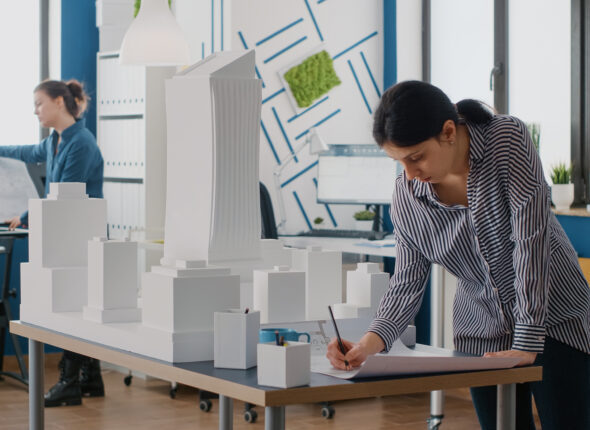 Woman architect analyzing blueprints plan on table to design building model and maquette